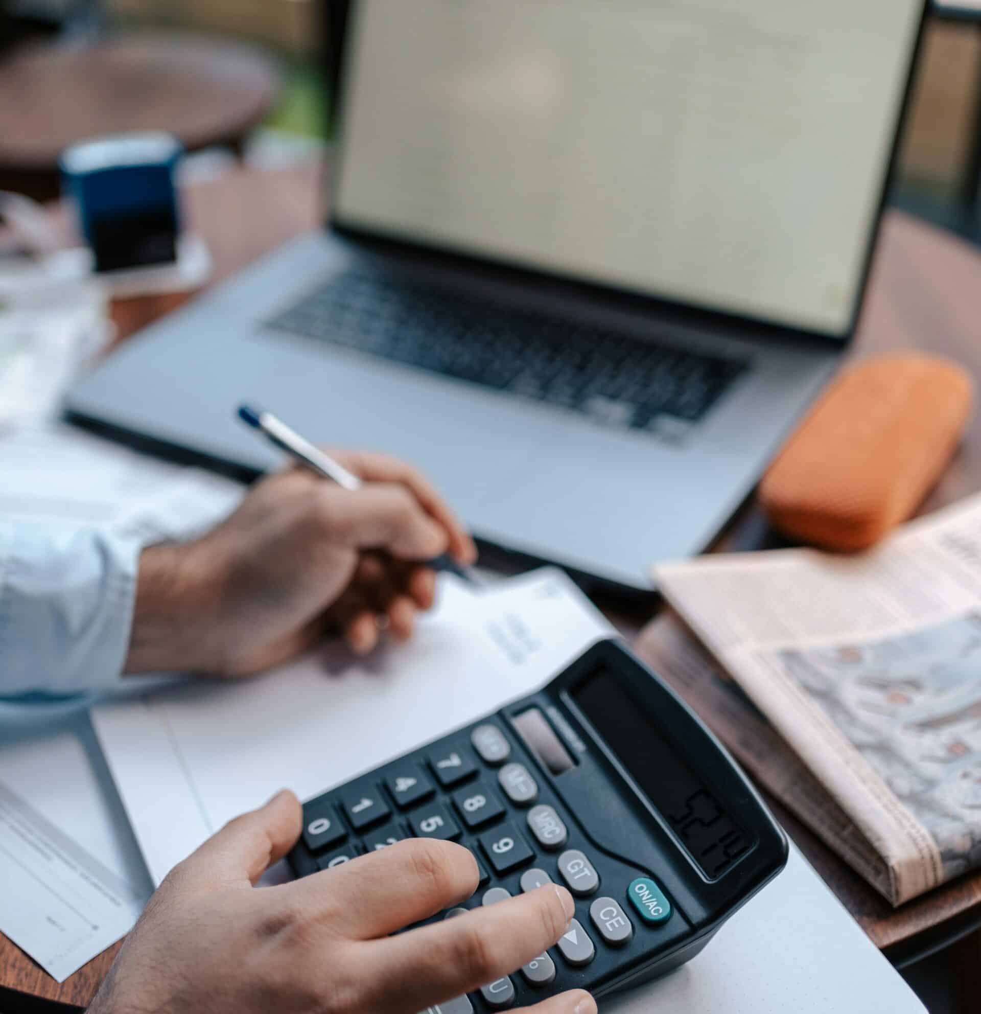 Person working on financial documents with laptop and calculator.