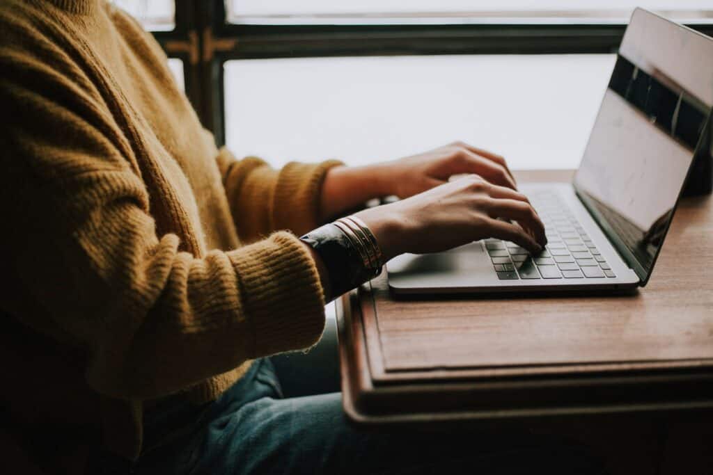 Person typing on a laptop at a wooden desk in a cozy setting.
