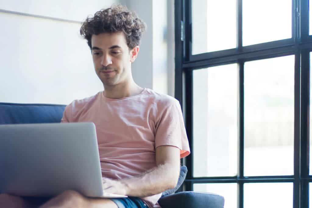 Young man using a laptop near a large window in a modern home.