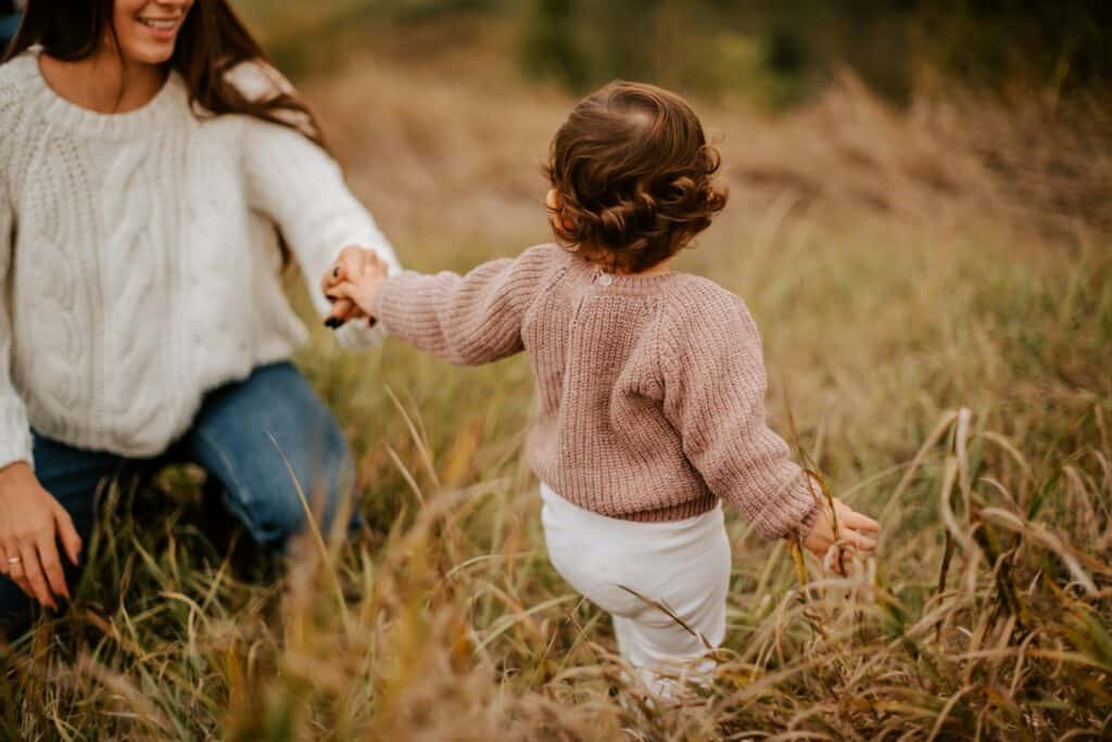 Mother and child holding hands in a grassy field during autumn.