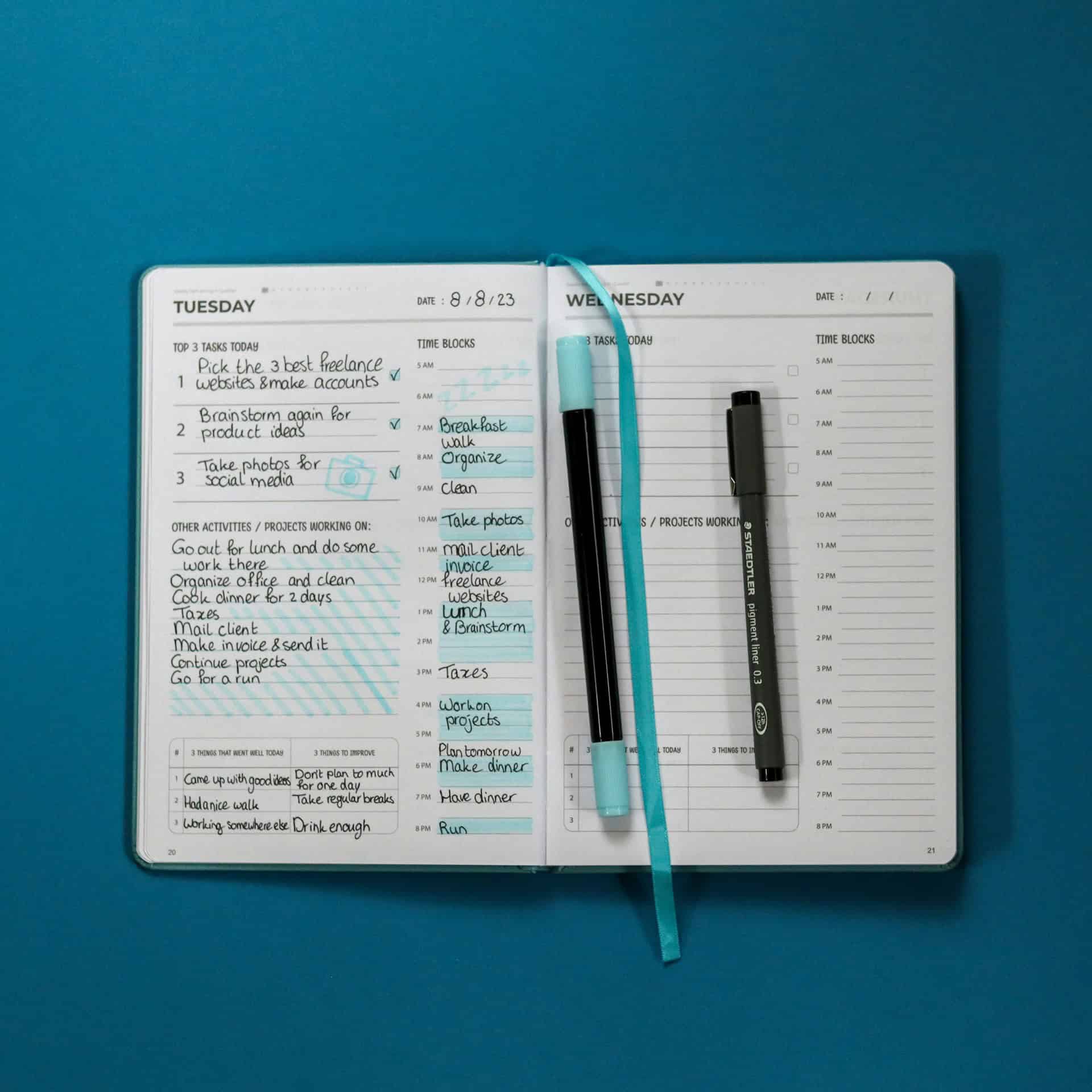 Open planner with weekly schedule and notebook with pens on blue background.