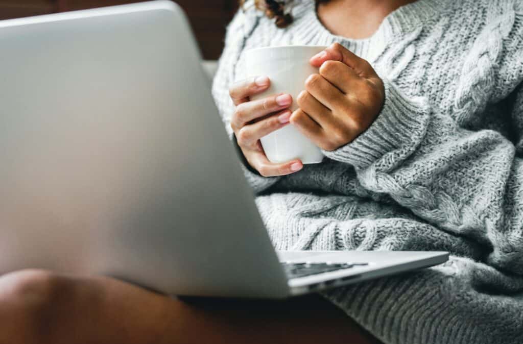 Woman holding coffee mug while working on a laptop.